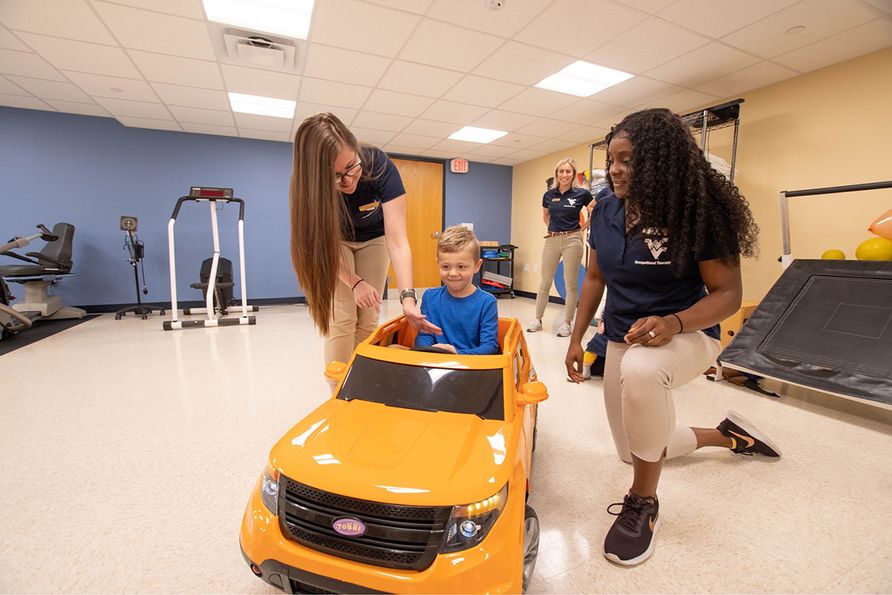 WVU Division of Occupational Therapy graduates (from left) Lexi Bailey, Emily Hvizdak and Ashlyn Richardson work with Noah Woods (at center) as part of the Go Baby Go project. (WVU Photo)